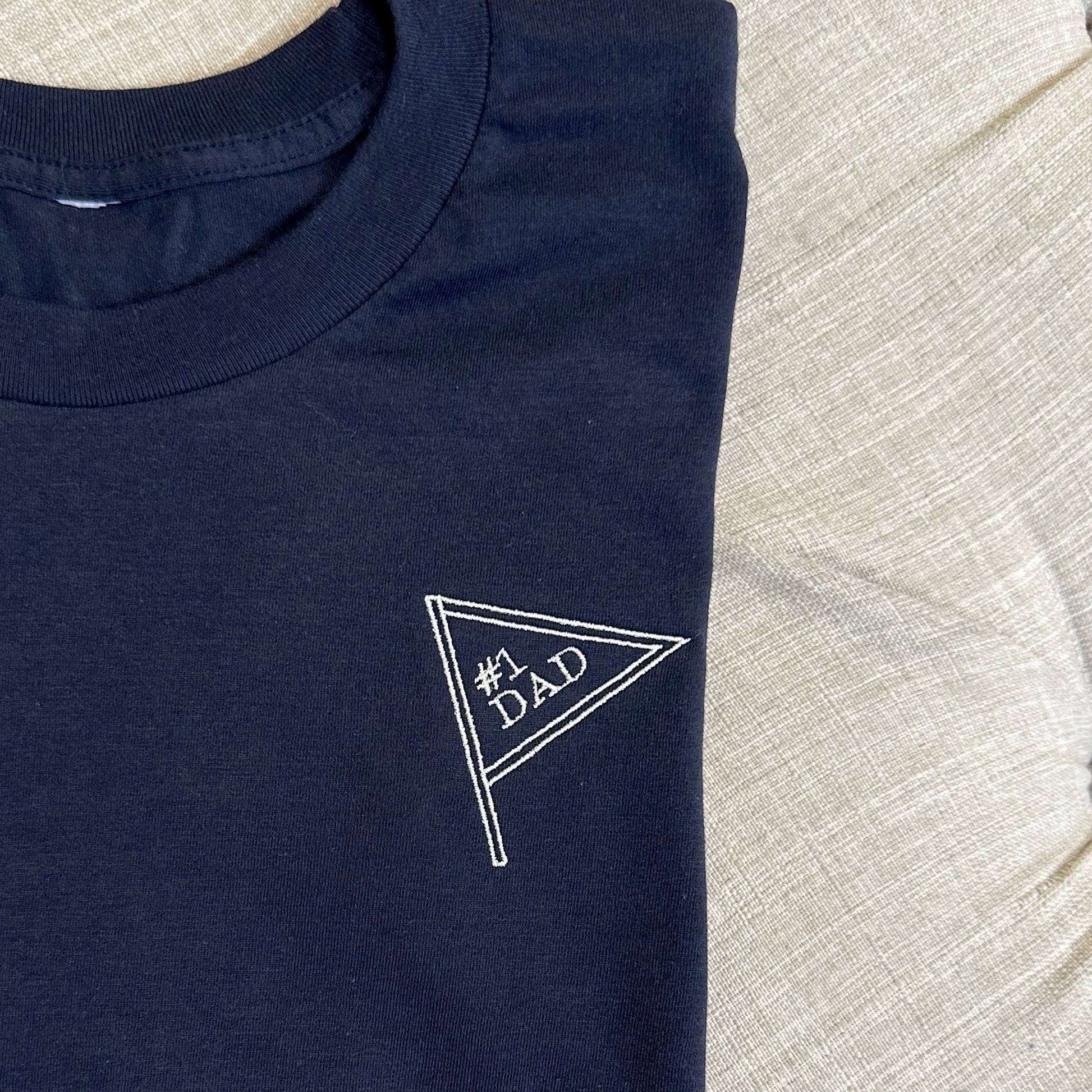 close up of embroidered navy tee with #1 dad inside a mini pennant
