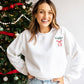 woman standing by a christmas tree wearing a white pullover sweatshirt with a custom name and ribbon bow embroidered on the left chest