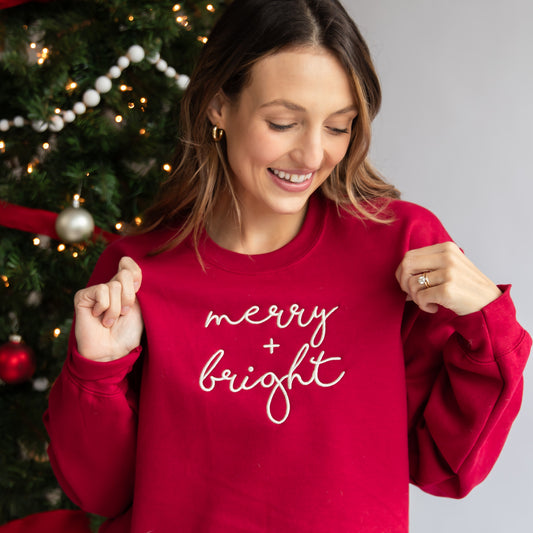 woman wearing a red crewneck sweatshirt with merry and bright embroidered across the chest