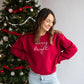 woman standing near a festive christmas tree with a red merry and bright crewneck sweatshirt
