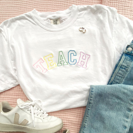 white comfort colors t-shirt with embroidered teach in pastel rainbow thread styled with jeans and sneakers