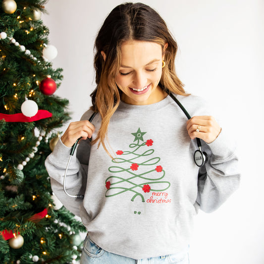 nurse wearing a gray crewneck sweatshirt with a christmas tree stethoscope design and merry christmas printed on the front
