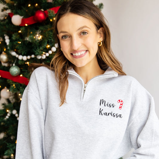 woman wearing a gray quarter zip with miss karissa embroidered in a script font next to an embroidered mini candy cane