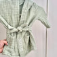 Green textured robe with 'NOAH' embroidery held by a hand against a neutral background