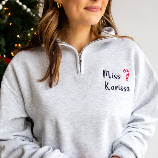 close up of a teacher wearing a quarter zip with a personalized name and festive candy cane embroidery design on the left chest