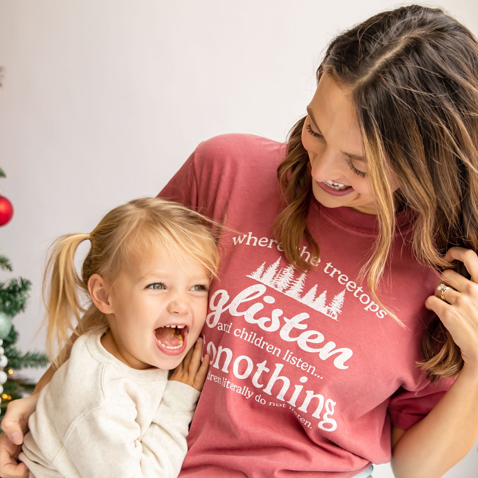 woman and her daughter laughing, woman wearing a short sleeve comfort colors t-shirt with a funny christmas print about children not listening on the front