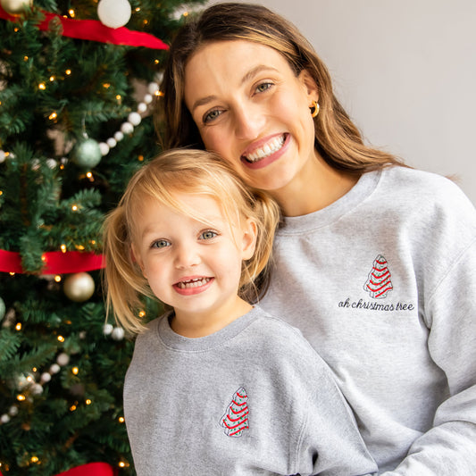 little girl and her mom wearing matching christmas sweatshirts with custom little debbie embroidered designs on the left chest