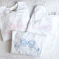 stack of white tees with outlined bow designs embroidered on the front center