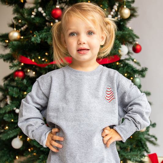 little girl wearing a gray crewneck sweatshirt with custom little debbie christmas tree design on the left chest