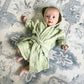 Baby wearing a green hooded robe on a patterned rug