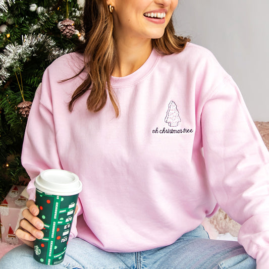 woman wearing pink sweatshirt with white little debbie christmas tree embroidered on the left  chest