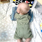 baby boy wearing 2 piece olive set including a bodysuit and matching shorts. he's laying on his belly on a playmat looking at a black and white book