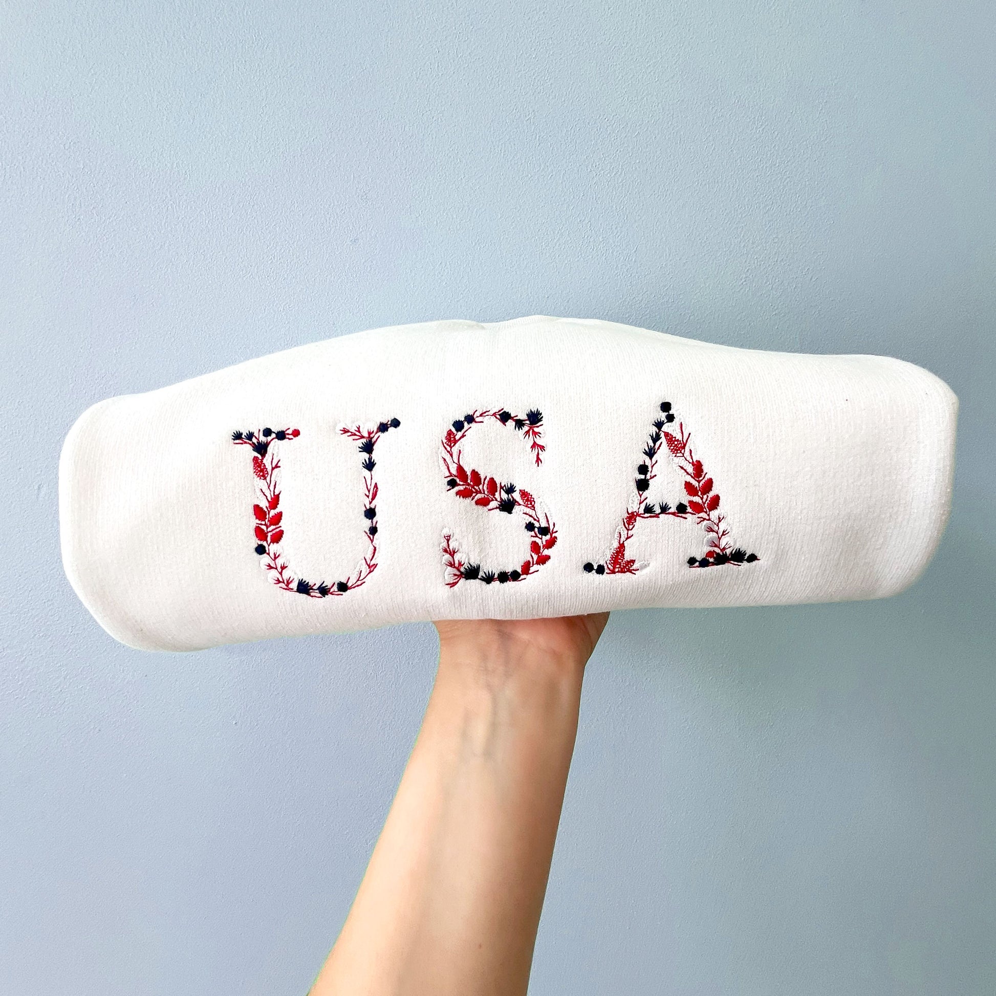 a white crewneck sweatshirt with embroidered USA floral design in red, white and navy threads.