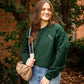 woman outside wearing a dark green pullover sweatshirt with a personalized monogram embroidered on the left chest