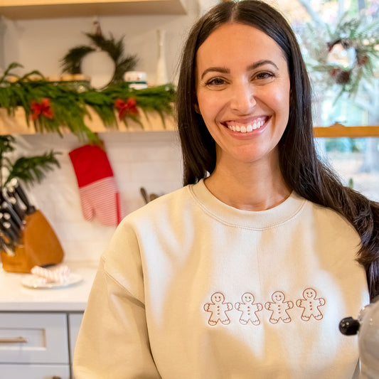 woman standing in a christmas decorated crewneck with gingerbread men decorated across the chest