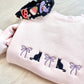 Blush pink sweatshirt with black cat and bow embroidered design across the chest, paired with a  decorative Halloween headband.