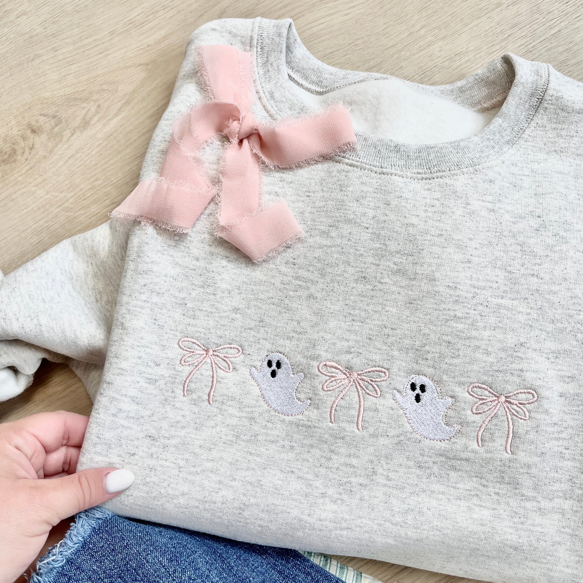 Ash sweatshirt with embroidered ghosts and bows across the chest. paired with jeans and a blush pink ribbon bow