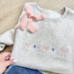 Ash sweatshirt with embroidered ghosts and bows across the chest. paired with jeans and a blush pink ribbon bow