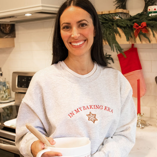 woman standing in her kitchen baking wearing an in my baking era crewneck sweatshirt