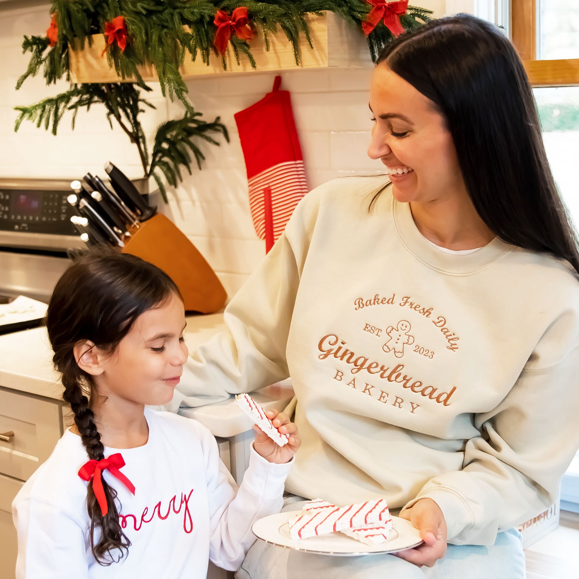 mother and daughter in their kitchen eating christmas cookies wearing festive christmas sweatshirts