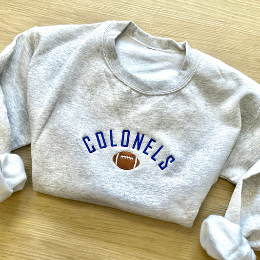 ash sweatshirt with custom embroidery featuring a mascot name in a curved design centered above an embroidered football icon. 