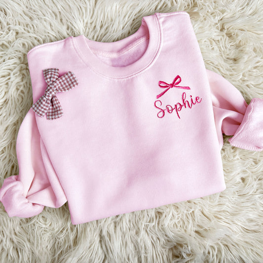 pink youth crewneck sweatshirt with embroidered bow and name design on the left chest in pink thread 