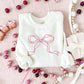 Christmas styled flat lay of a sweet cream crewneck with embroidered ribbon bow design in pink thread large across the chest