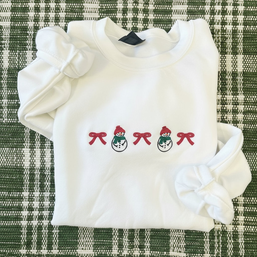 White sweatshirt with embroidered bow and snowmen designs on a plaid fabric background