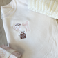white crewneck with custom coquette gingerbread embroidery on the left chest