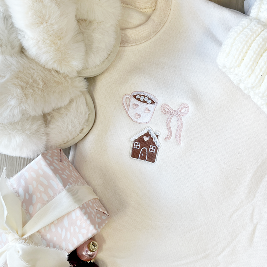 Close-up of a white garment with embroidered designs, including a teacup, gingerbread house, and bow.