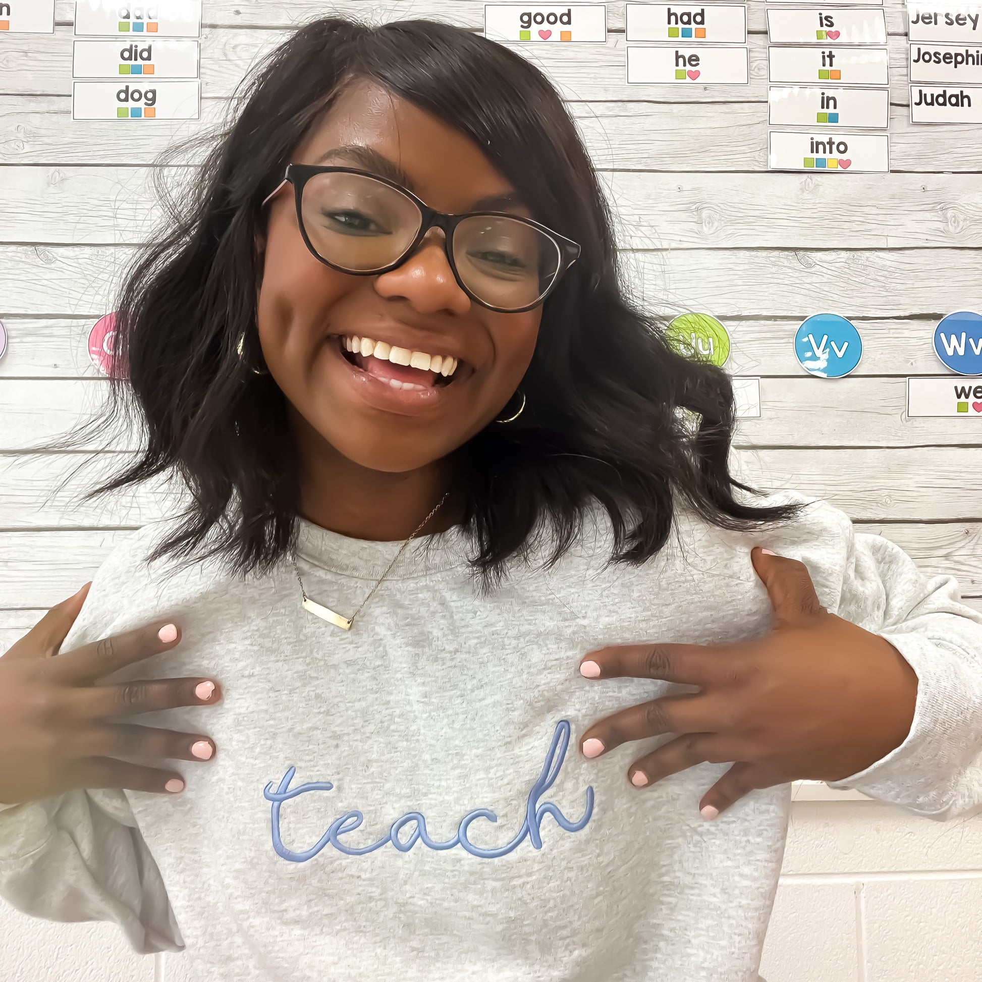 teacher wearing ash grey crewneck with teach embroidered across the chest