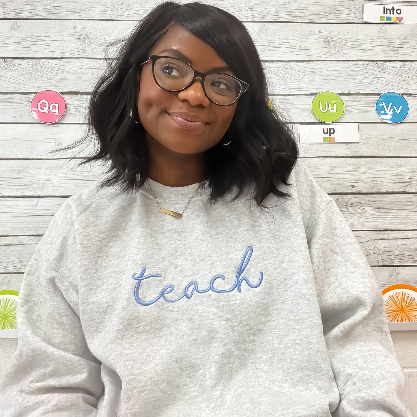 teacher wearing ash sweatshirt with embroidered teach design in periwinkle thread