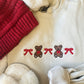 Beige sweatshirt with embroidered teddy bears and red bows, surrounded by red knitted item and white fabric.