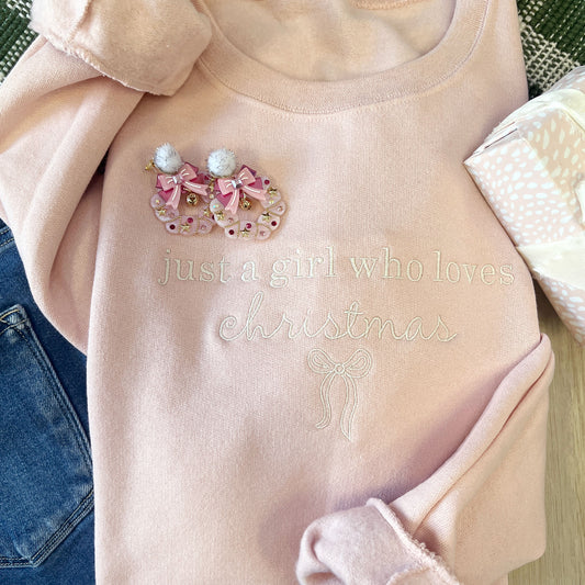 Pink sweater with Christmas-themed design and text 'just a girl who loves Christmas' on a neutral background.