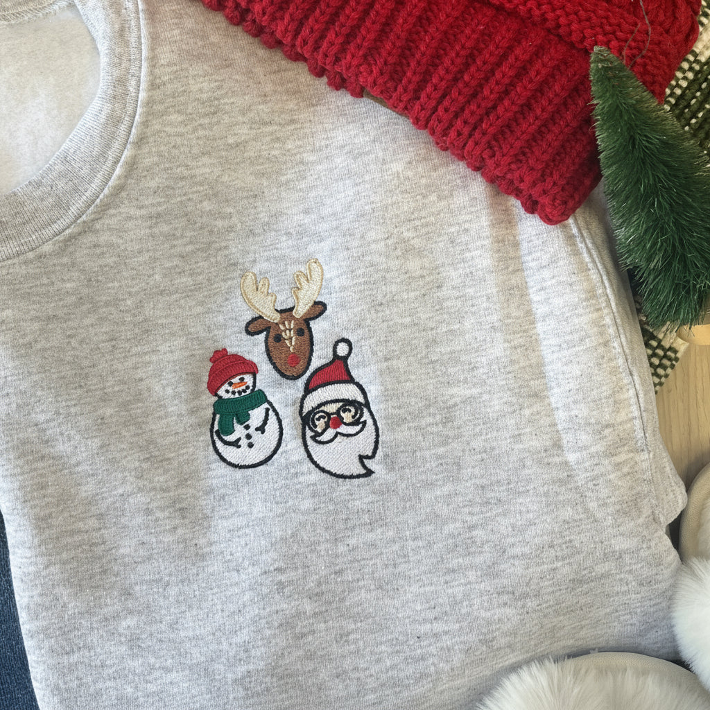 Gray sweatshirt with Christmas-themed embroidery of a snowman, reindeer, and Santa Claus on a red fabric background.