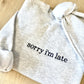 Gray sweatshirt with 'sorry i'm late' embroidered in navy thread on a wooden surface