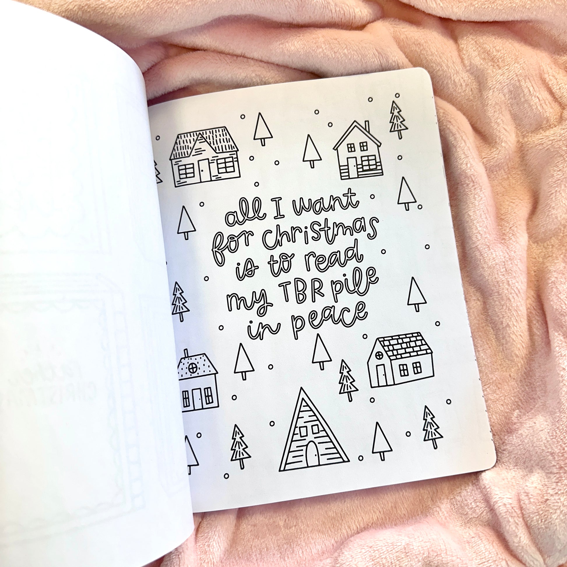 Notebook page with text 'all I want for Christmas is to read my TBR pile in peace' surrounded by house and tree illustrations on a soft pink background.