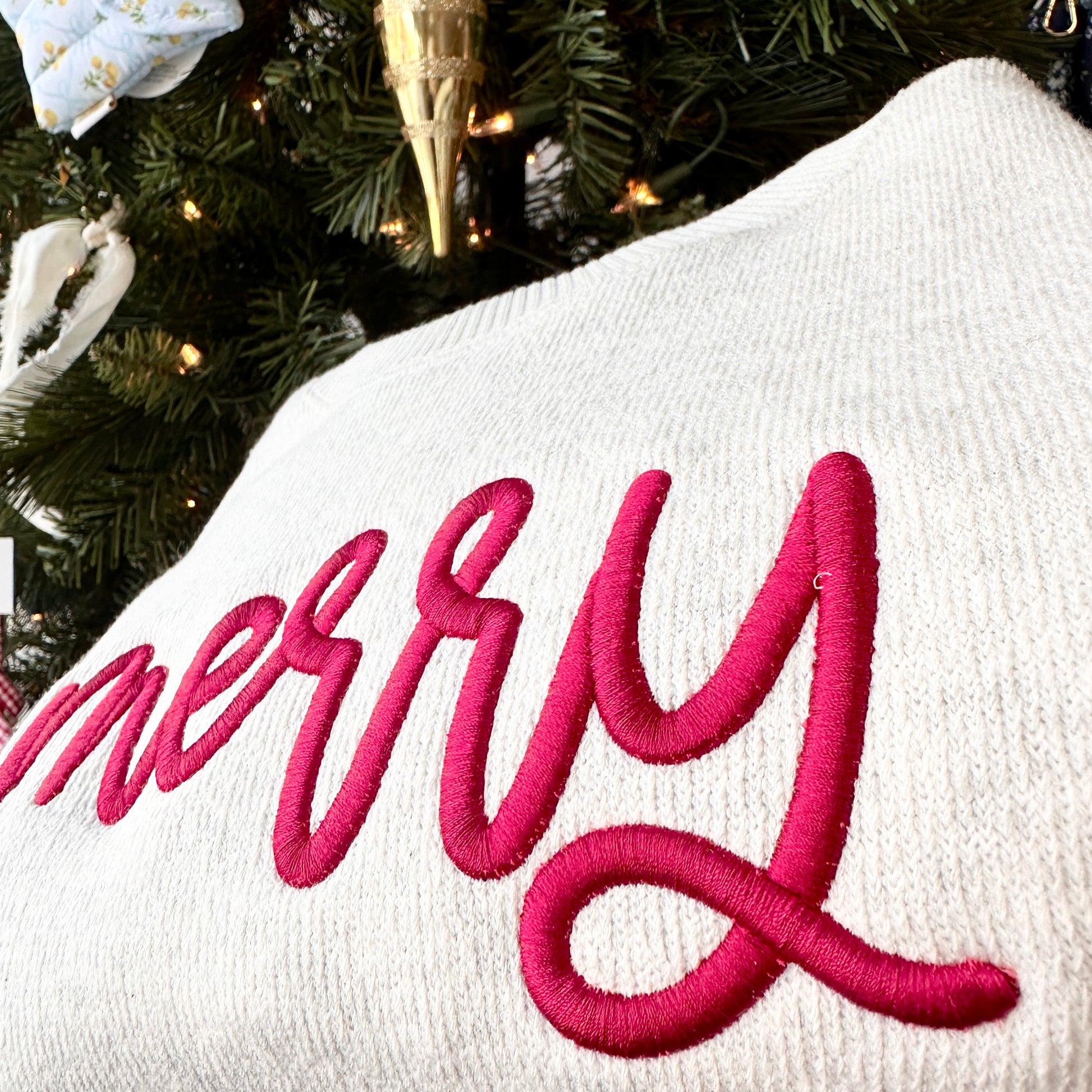 White sweatshirt with red 'Merry' text in front of a decorated Christmas tree.
