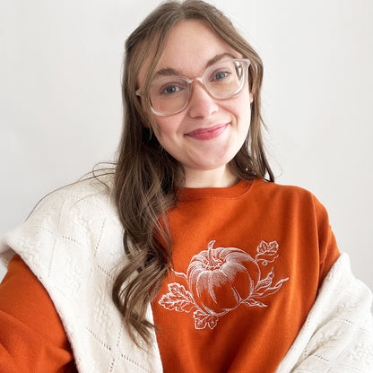 young woman wearing an embroidered texas orange crewneck sweatshirt with a stitched vintage pumpkin design