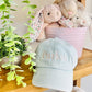 Light blue cap with 'Parker' embroidered on it, placed on a wooden surface with stuffed animals and plants in the background.