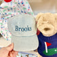 Light blue cap with 'Brooks' embroidery held by a hand, next to a teddy bear in a colorful outfit.