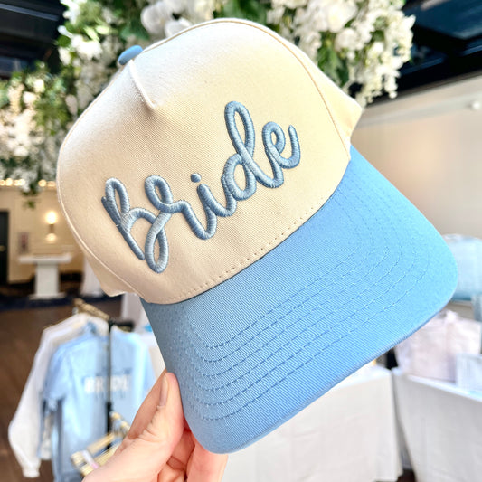 Beige and blue cap with 'Bride' embroidery held in front of a blurred indoor background.