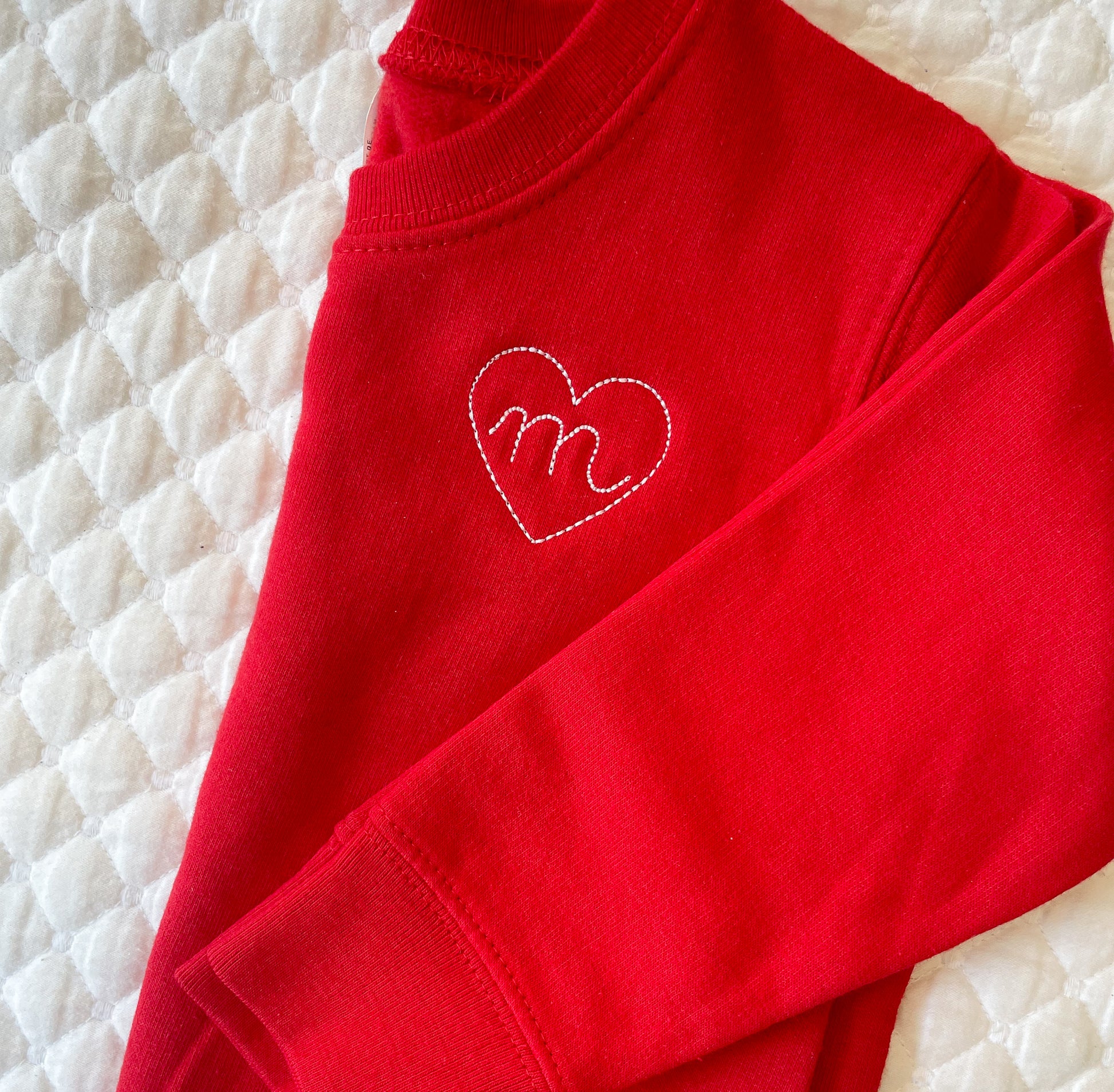 closeup of red toddler crewneck sweatshirt with stitched heart and initial design on the left chest