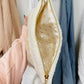Close-up of a cream-colored pouch with gold zipper held in front of clothes.