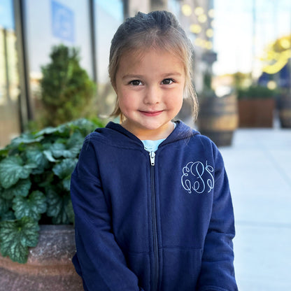 little girl wearing a navy blue full zip jacket with custom embroidered monogram in a periwinkle thread