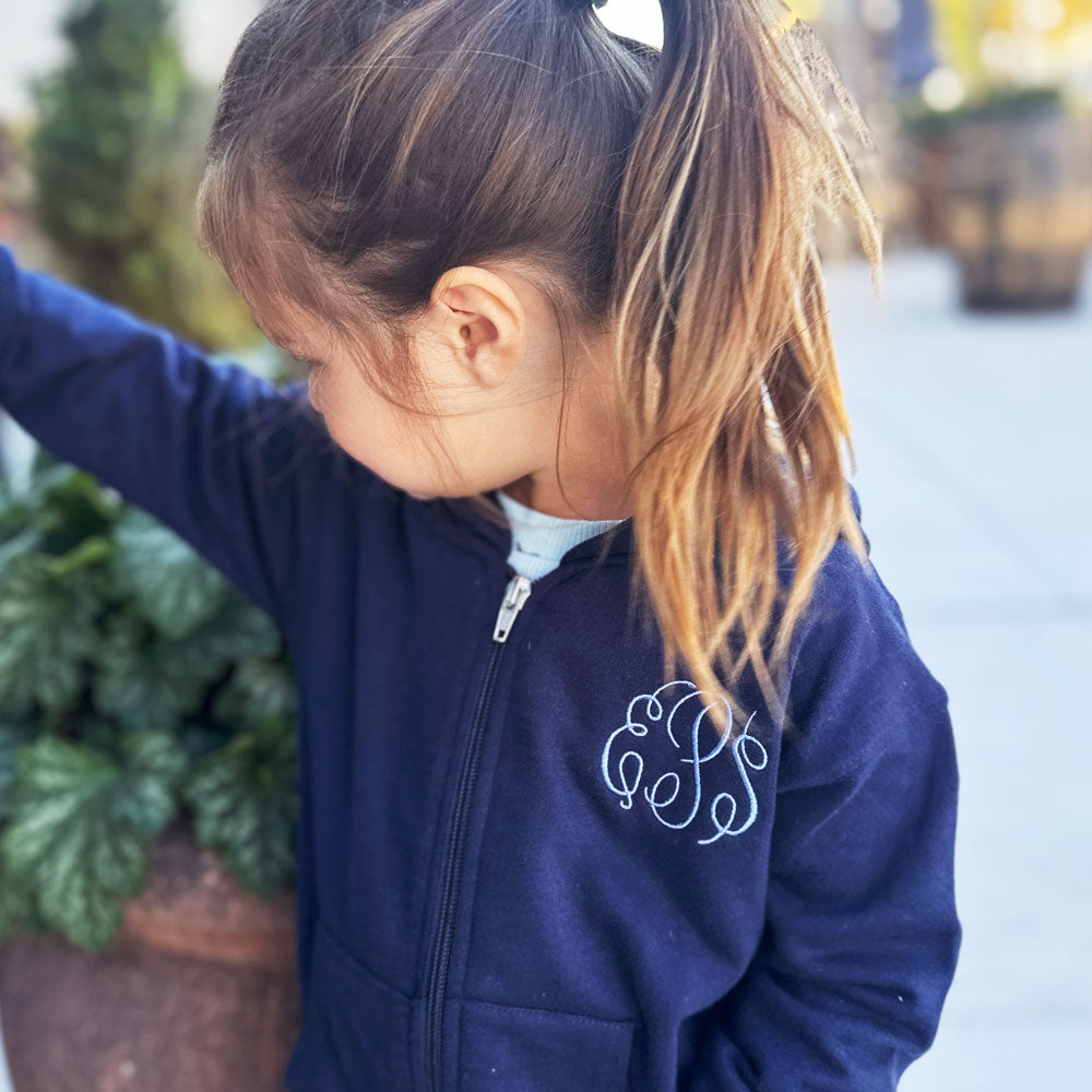 little girl wearing a navy blue full zip jacket with custom embroidered monogram in a periwinkle thread