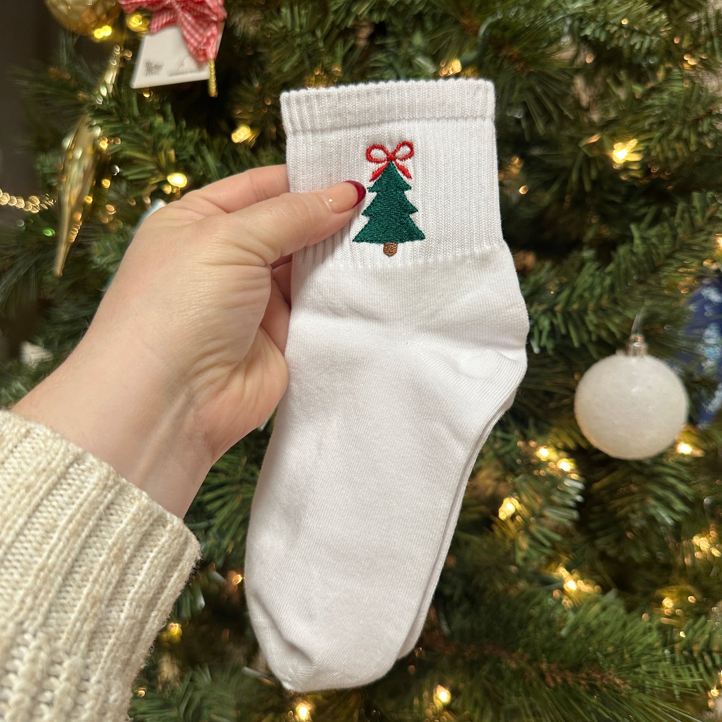 White socks with Christmas design held in front of a decorated Christmas tree.