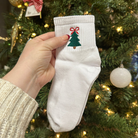 White socks with Christmas design held in front of a decorated Christmas tree.