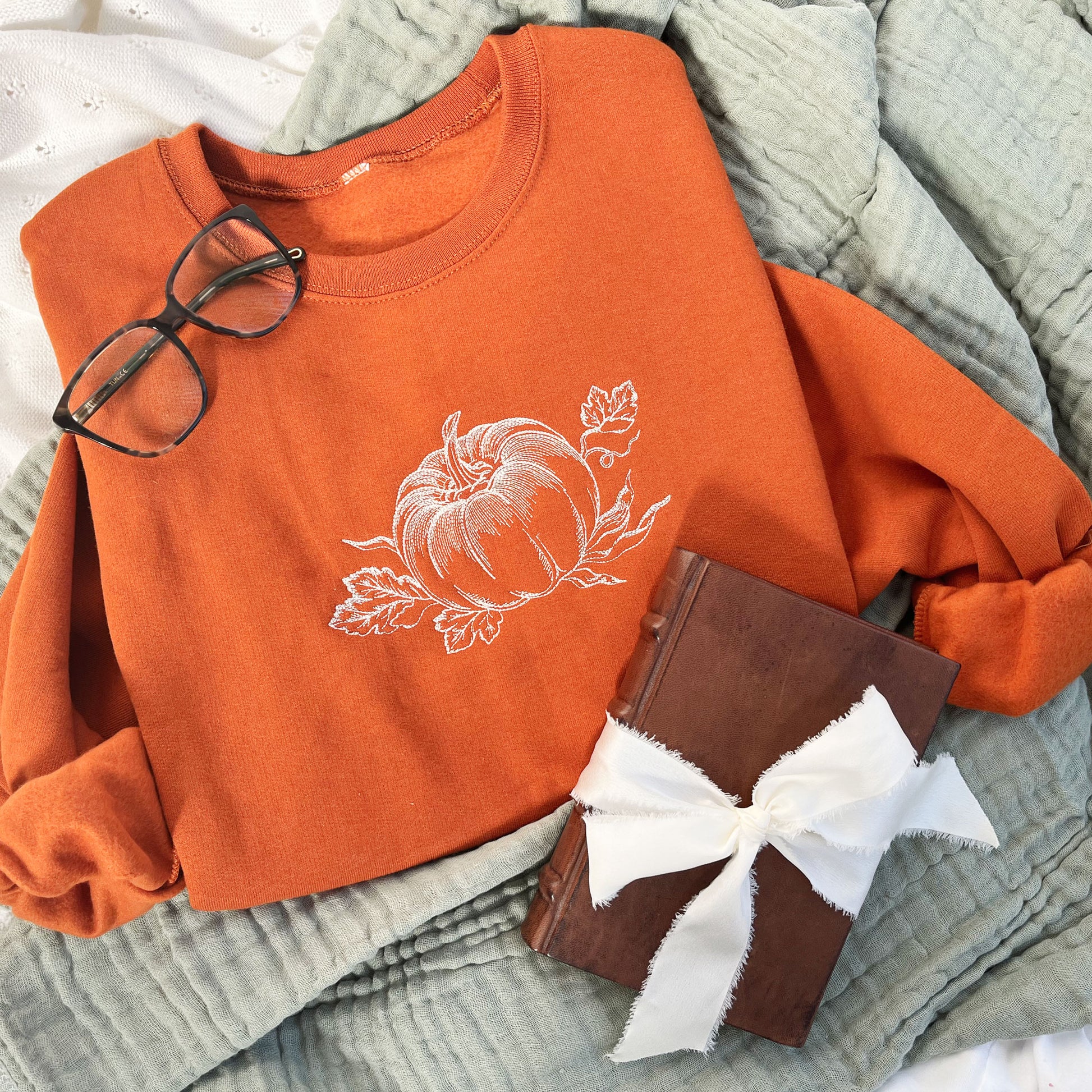 styled flat lay photo of an embroidered texas orange crewneck sweatshirt with a stitched vintage pumpkin design