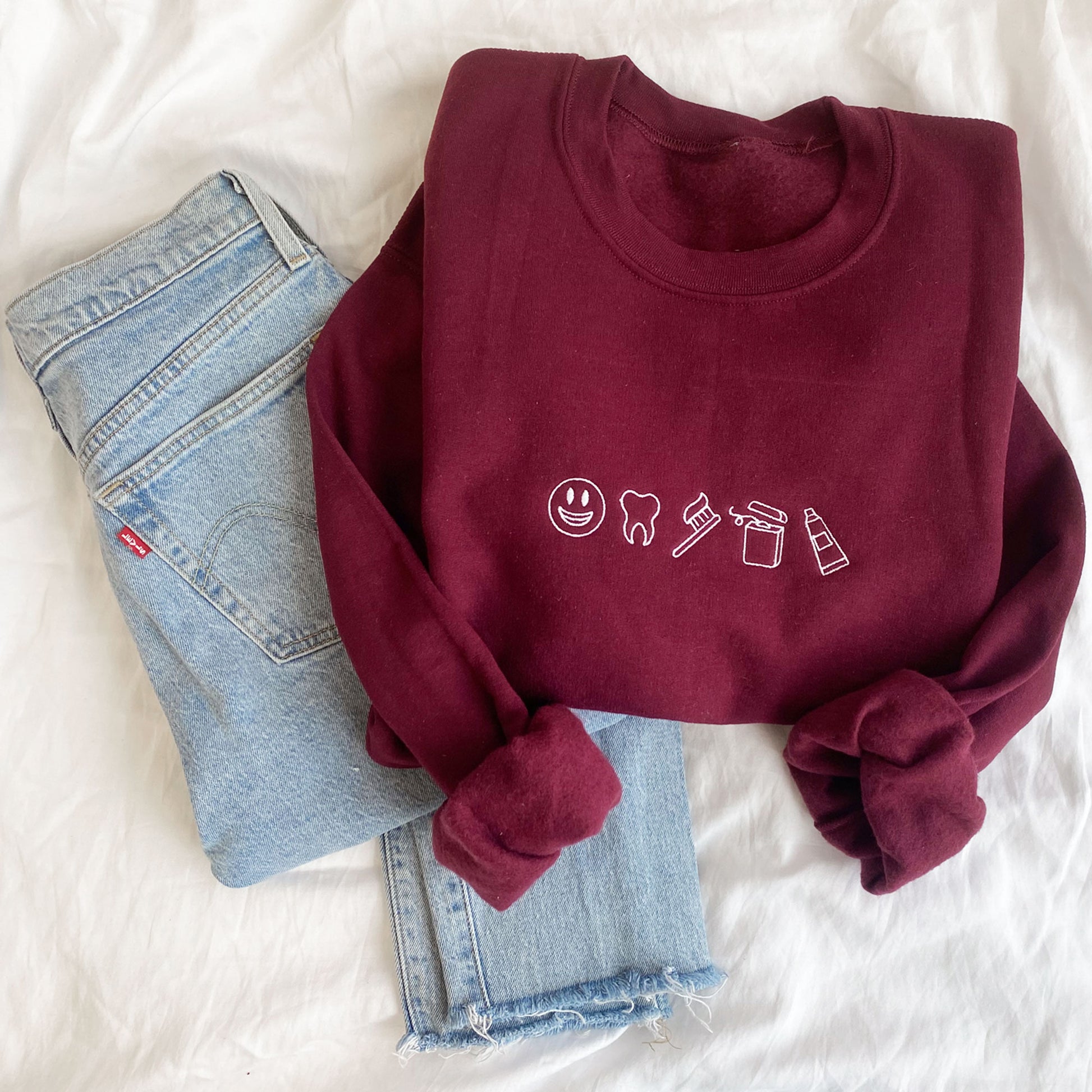 maroon crewneck sweatshirt with embroidered mini dental icons across the chest in white thread styled with blue jeans